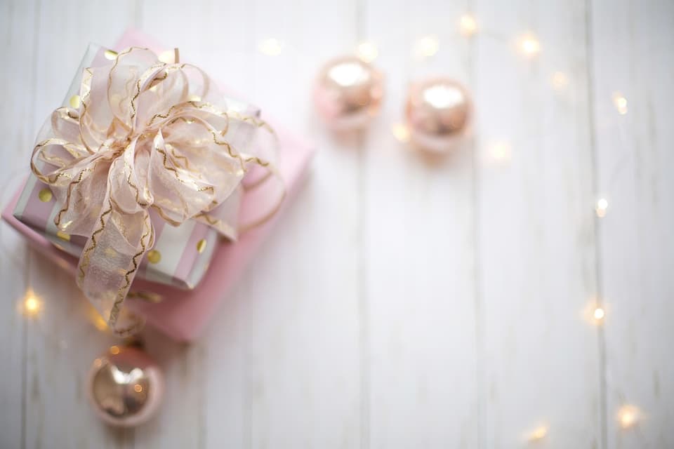 Stacked pink gift boxes with a gold ribbon, ornaments, and fairy lights